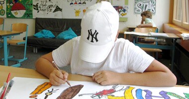 Ein Schüler in einem weißen Käppi malt ein buntes Bild